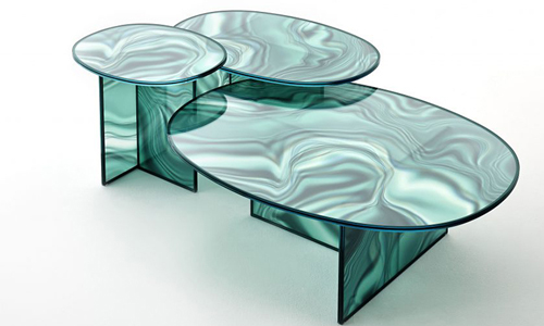 Liquefy son mesas altas y bajas de forma ovalada en vidrio templado, con decoración descolorida e irregular que adquiere el color y las vetas del mármol.